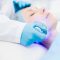 Gloved cosmetician holding electric device while making beauty procedure on client face